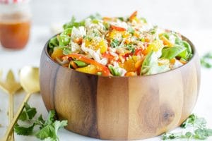 A wooden bowl packed with an Asian Cabbage Salad and a jar of asian cabbage salad dressing.