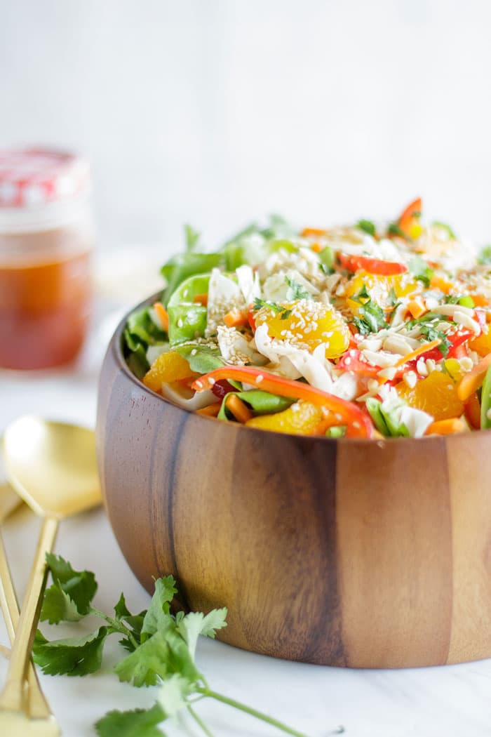 A wooden bowl packed with an Asian Cabbage Salad and a jar of asian cabbage salad dressing.