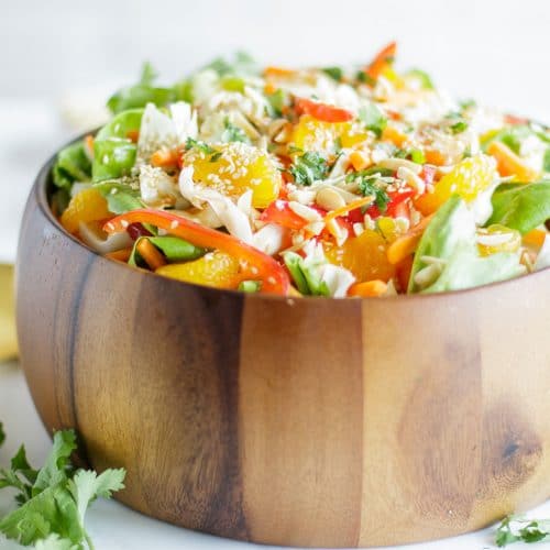 A wooden bowl packed with an Asian Cabbage Salad and a jar of asian cabbage salad dressing.