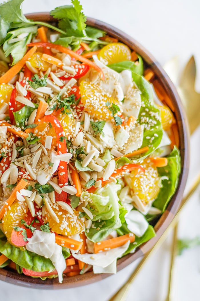 A close up of a  cabbage salad showing the variety of veggies, fruit and nuts.