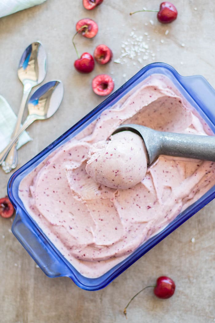 A blue glass container showing how to free cherry coconut sorbet to make nice scoops.