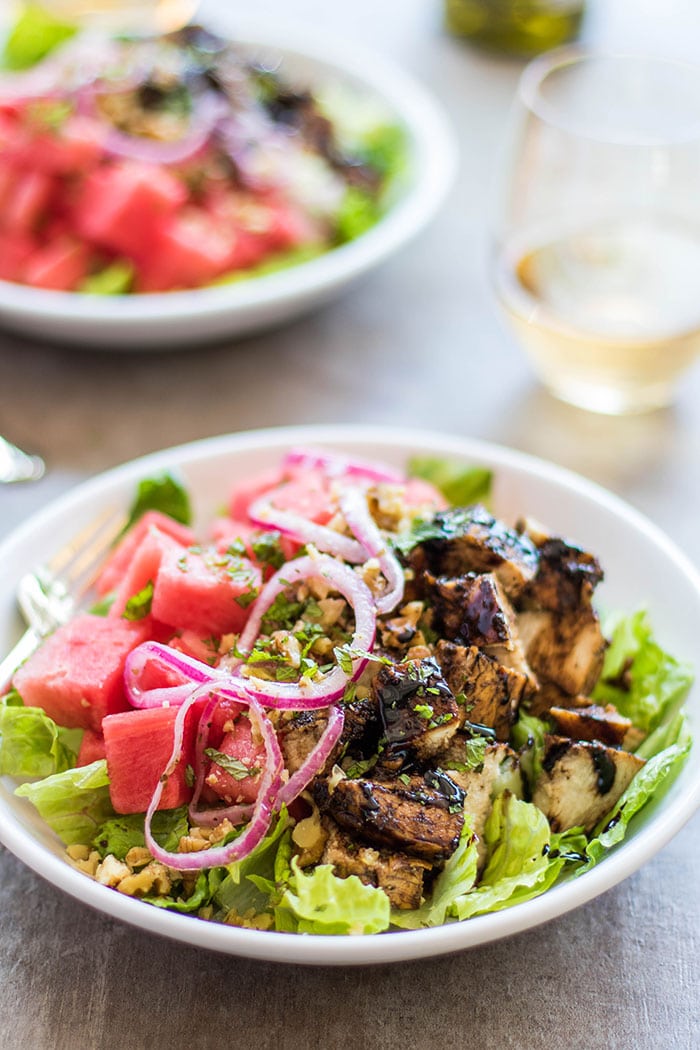 A plate piled high with a salad topped with grilled balsamic marinated chicken and watermelon.