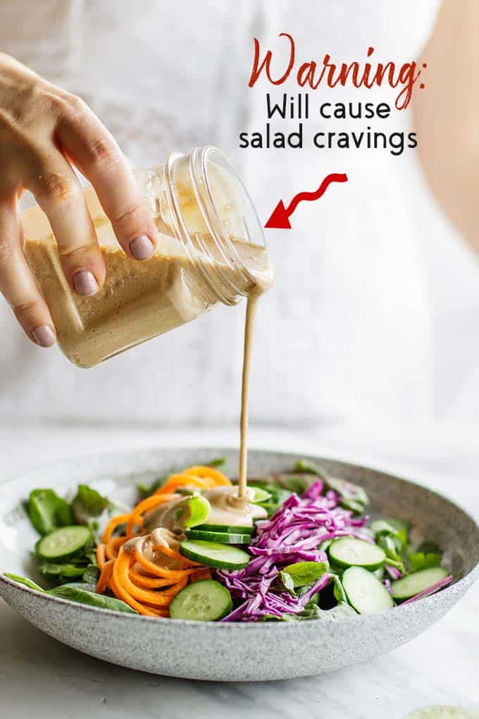 A salad bowl with spicy Thai almond salad dressing being drizzled on top.