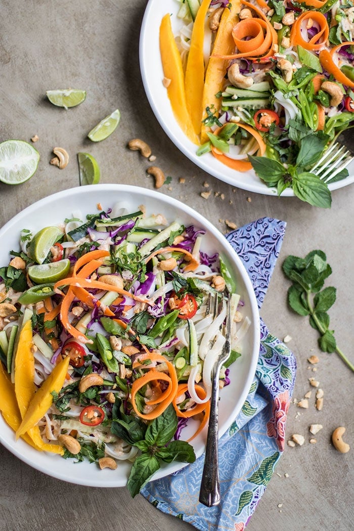 Two plates of Cold Thai Noodle Salad with cashews and limes around the plates.