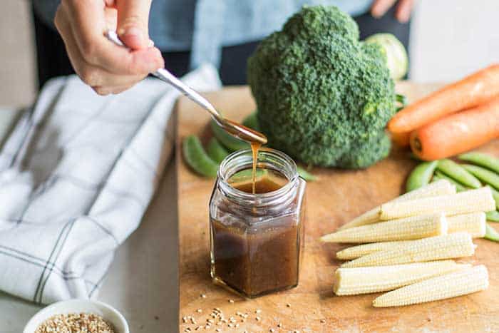 A cutting board with vegetables, and Michelle drizzling teriyaki sauce into a jar.