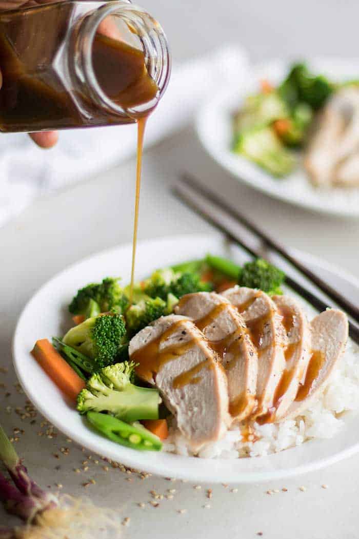 A plate of chicken, rice and vegetables, with soy free teriyaki sauce being drizzled on top.