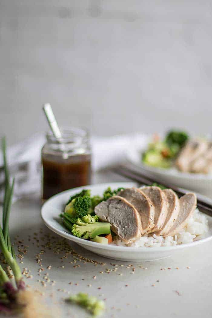 A plate with poached chicken on top of sauteed vegetables and rice.