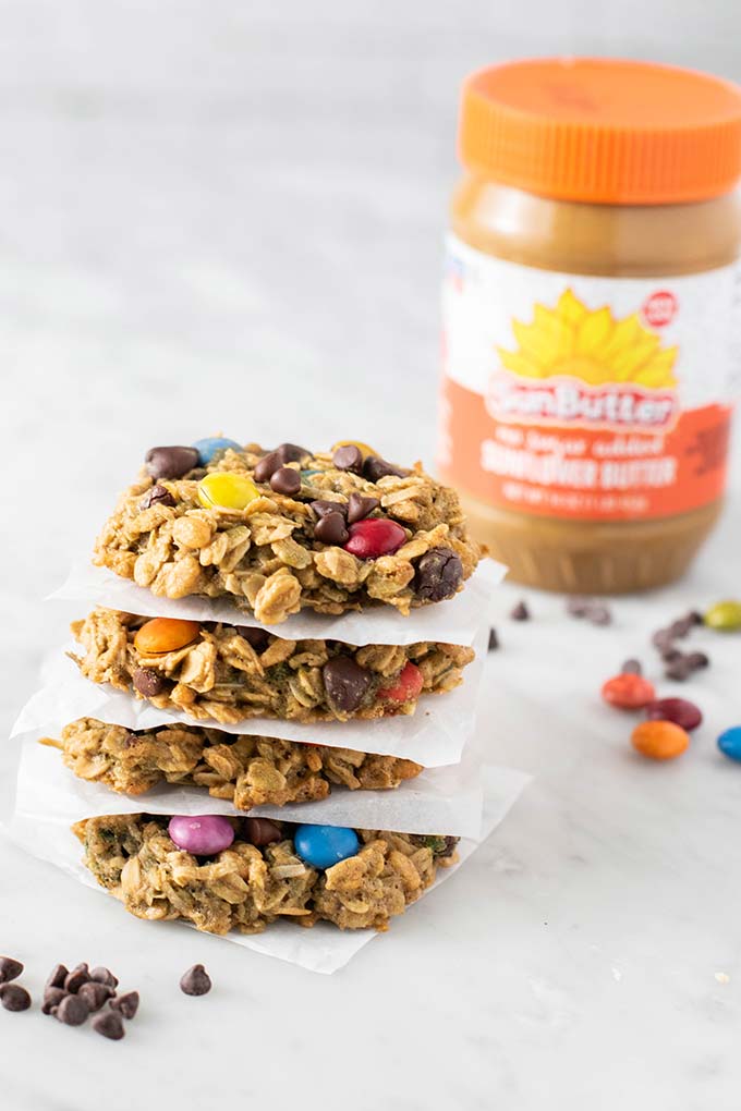 A stack of gluten free monster cookies surrounded by chocolate chips and colored chocolate pieces.