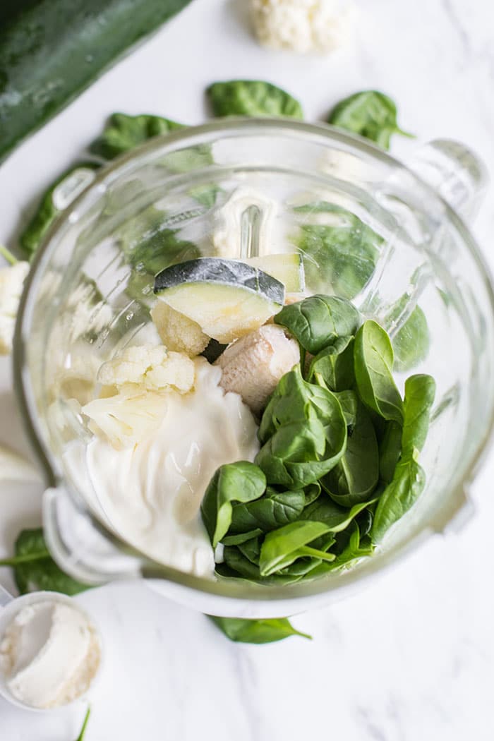 A glass blender with yogurt, spinach, zucchini and cauliflower.