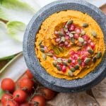 A stone bowl filled with a vibrant carrot hummus.
