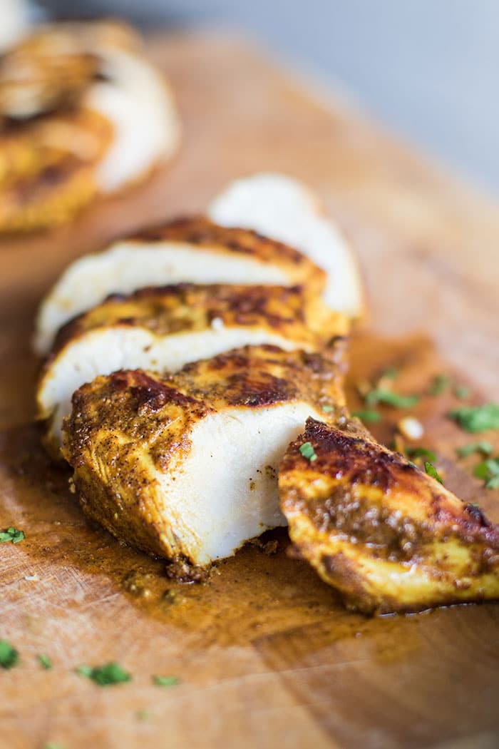 A cutting board with sliced moroccan spiced chicken breasts.