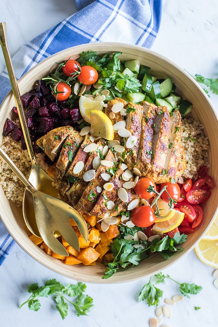 A top view of a quinoa salad loaded with cucumbers, tomatoes, herbs, roasted vegetables, and chicken.