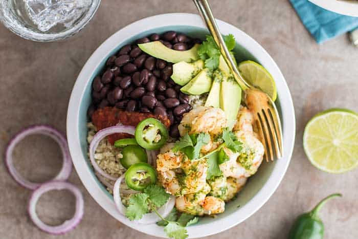 A top view of shrimp burrito bowls loaded with cauliflower rice, black beans, avocado, salsa and onions.