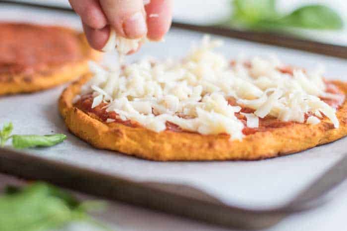Sprinkling cheese on top of a baked sweet potato pizza crust.