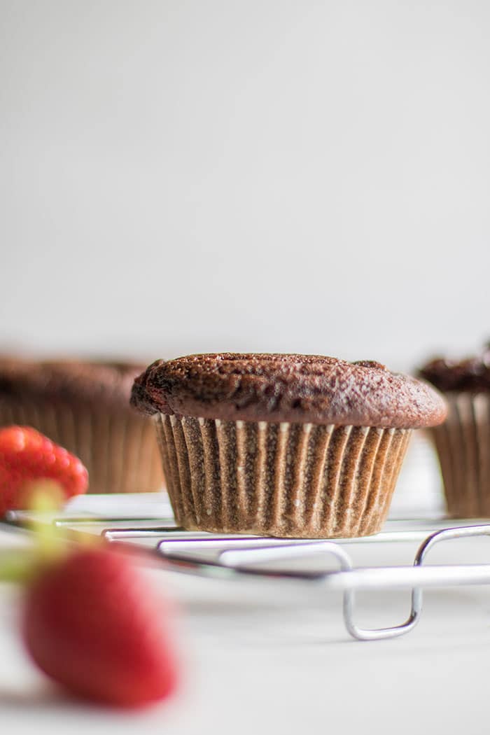 A chocolate cupcake surrounded by strawberries.