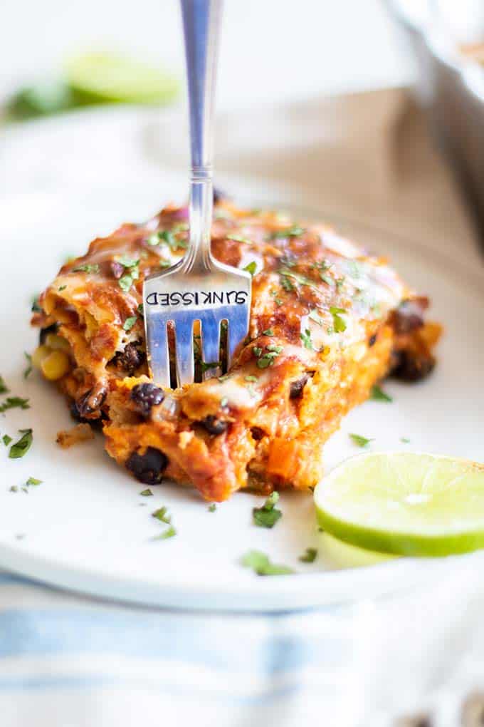 A slice of enchilada casserole with a fork sticking in to take a bite