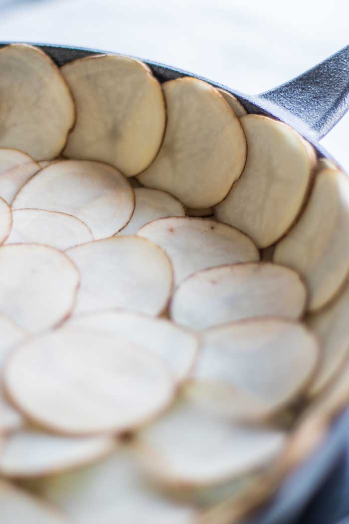 Thinly sliced potatoes arranged to form a crust in a cast iron skillet.