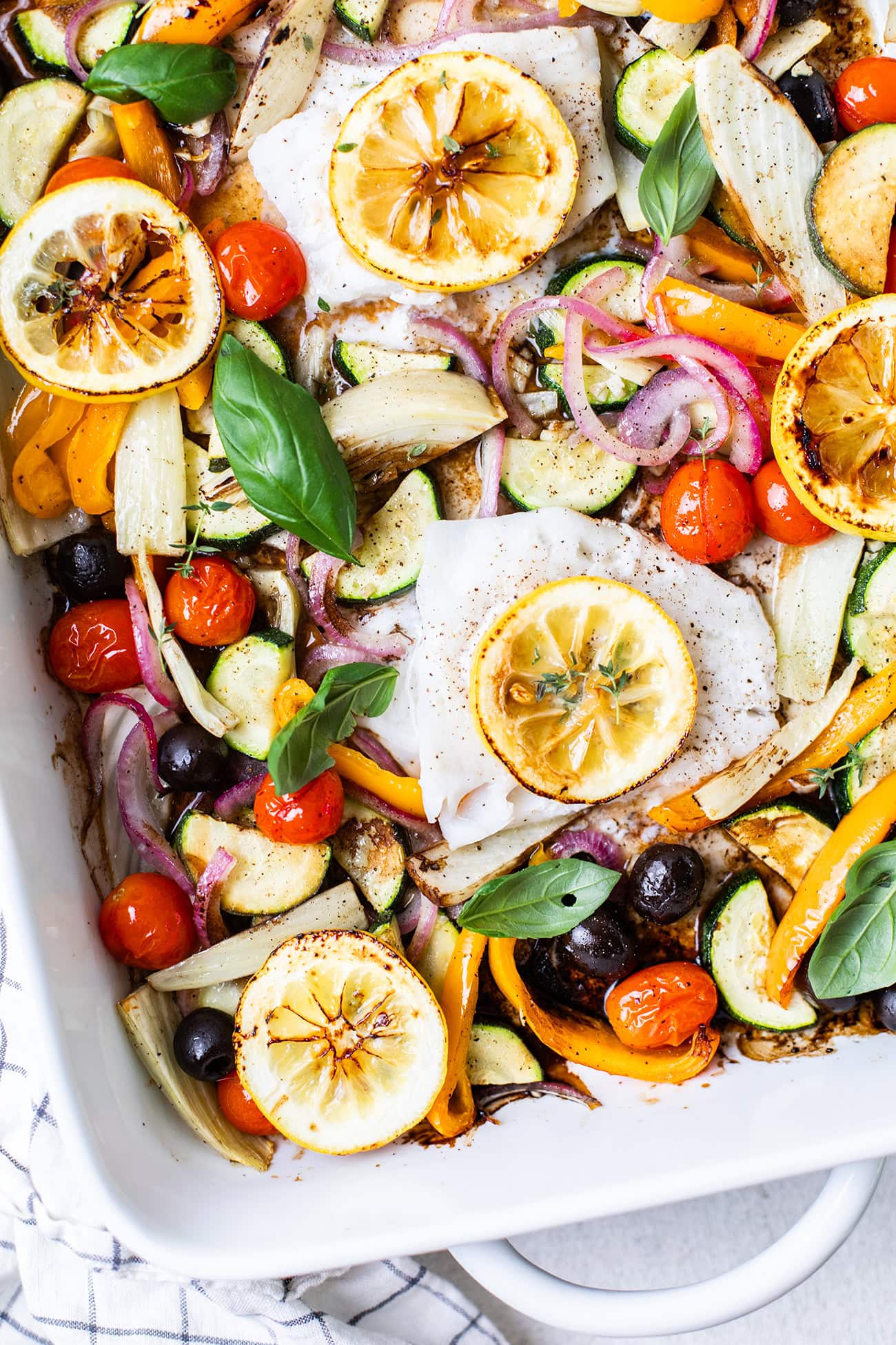 A baking dish filled with colorful vegetables and cod filets.
