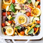 A close up look at a large baking pan with mediterranean baked cod and vegetables.