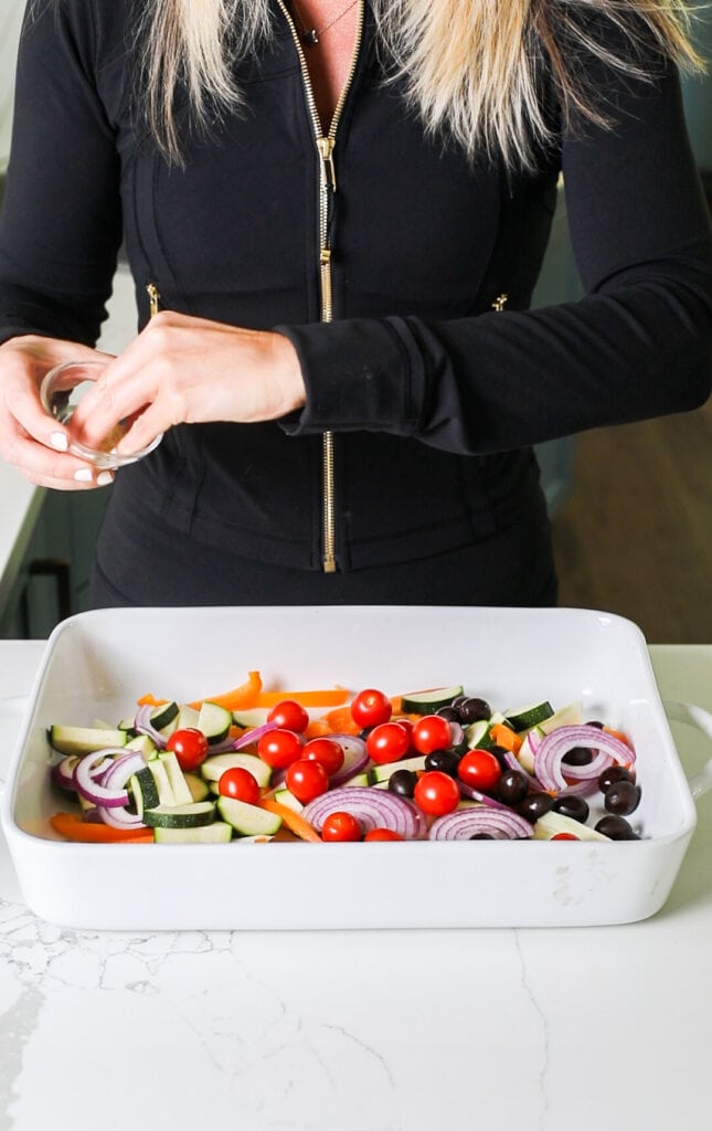 Seasoning vegetables in a large baking dish.