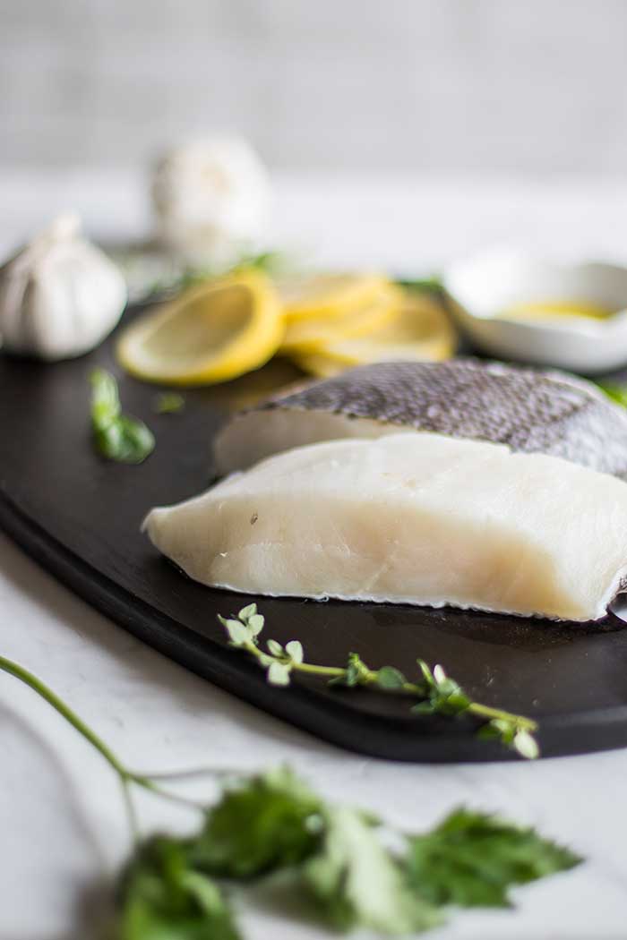 Two cod fillets on a cutting board with lemon and garlic.