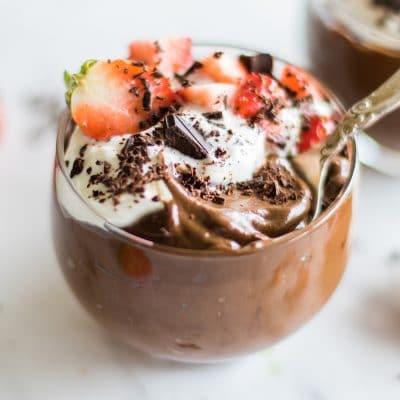 Two glasses filled with avocado chocolate pudding and strawberries.