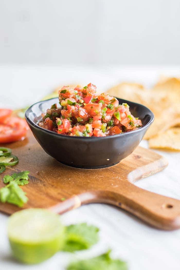 A bowl of salsa sitting on a cutting board.
