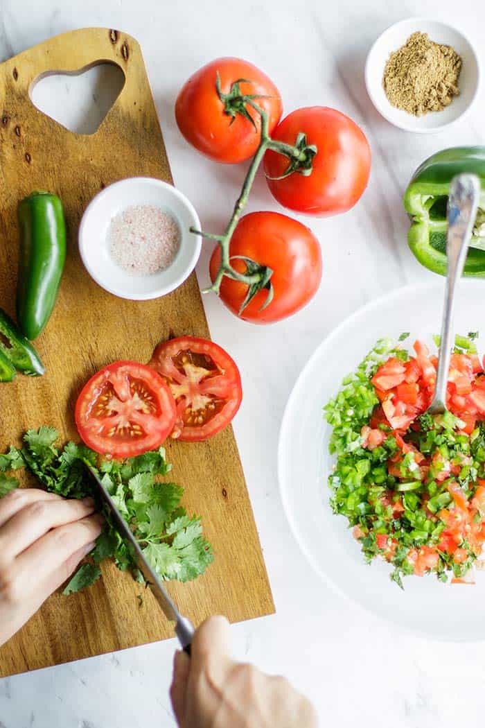 The ingredients for homemade salsa laying out on a cutting board being prepared for the recipe.