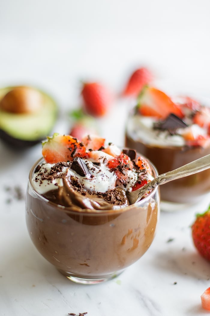 Two glasses filled with avocado chocolate pudding and strawberries.