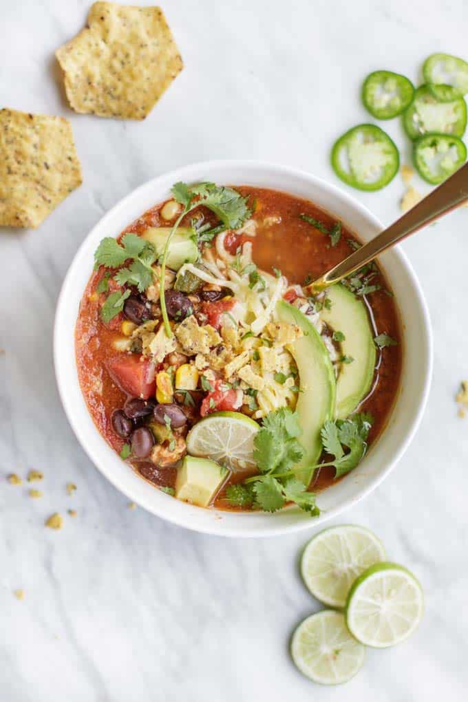 An overhead shot of a bowl of taco soup with avocado, cilantro and salsa on top.