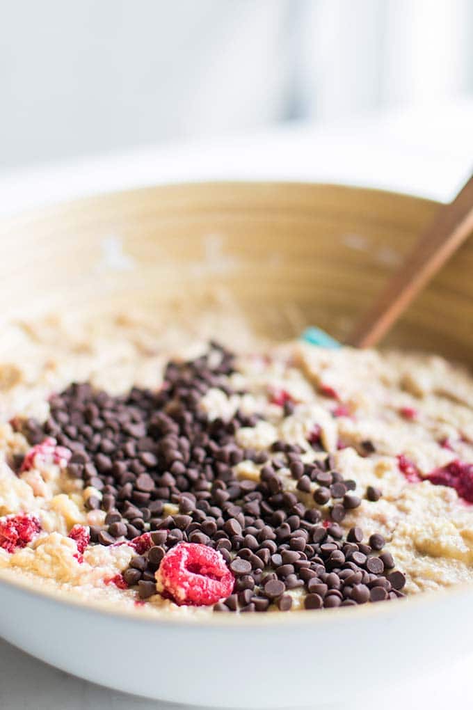 A mixing bowl showing raspberries and dark chocolate chips being mixed into the batter.