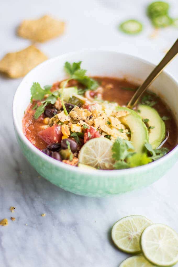 A bowl of this taco soup recipe with limes, chips, and jalapeno slices.