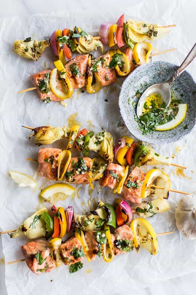Mediterranean salmon and artichoke skewers grilled and sitting next to a dish or parsley marinade.