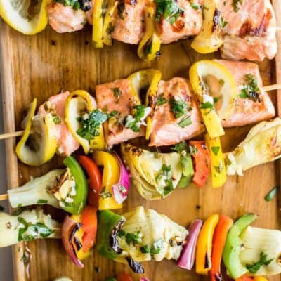 Grilled salmon and artichoke skewers shown up close drizzled with a parsley marinade.