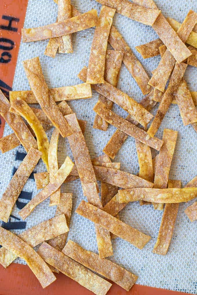Crunchy baked tortilla strips sprinkled with sea salt and cumin on a baking tray.