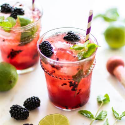 A side view of two clear glasses filled with blackberry mojitos.