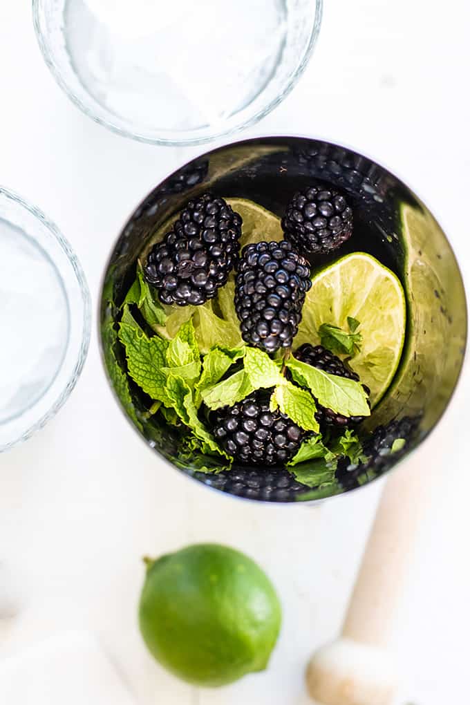 A view into a cocktail shaker filled with limes, mint and blackberries.