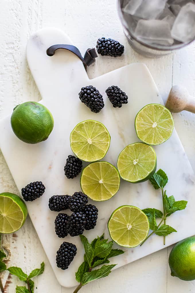 A cutting board with cut limes, mint and blackberries.