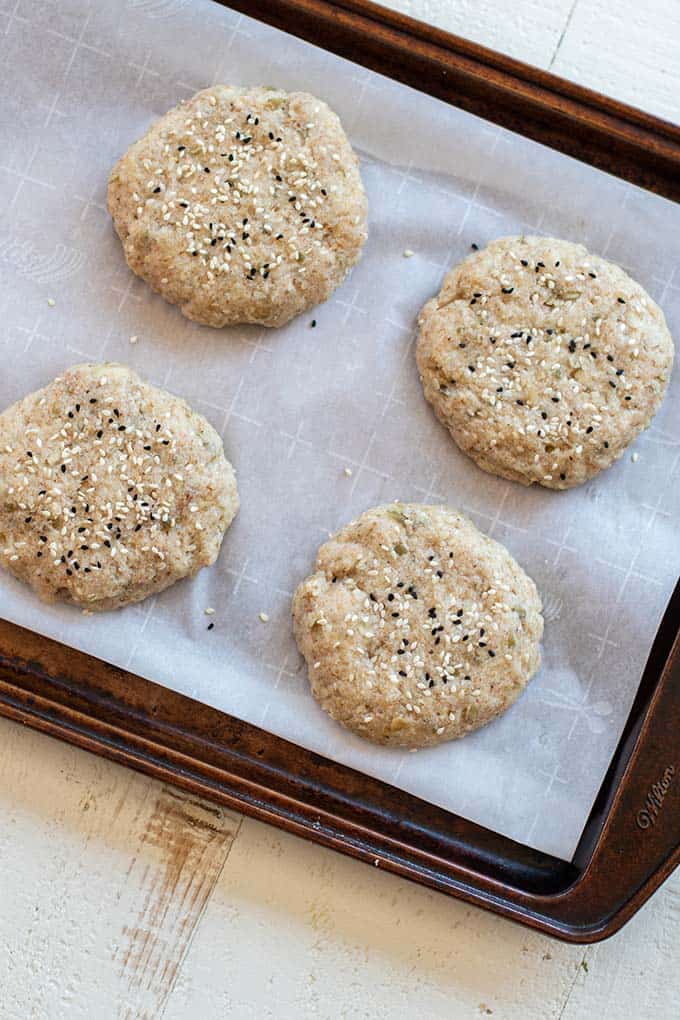 A baking pan with 4 mounds of dough topped with sesame seeds.