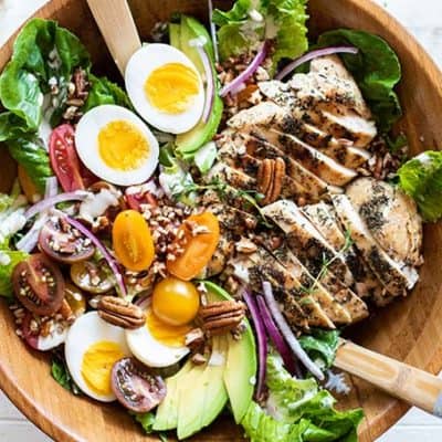 A top view of a crunchy whole30 chicken caesar salad topped with avocado, tomatoes, chicken, eggs and pecans.