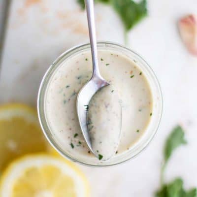 A jar of vegan caesar dressing with a spoon in it.