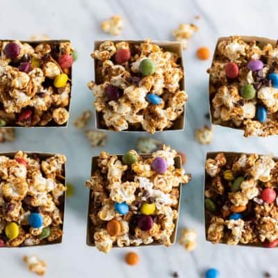 Looking down at 6 boxes of easy caramel corn with colorful candy pieces mixed in.