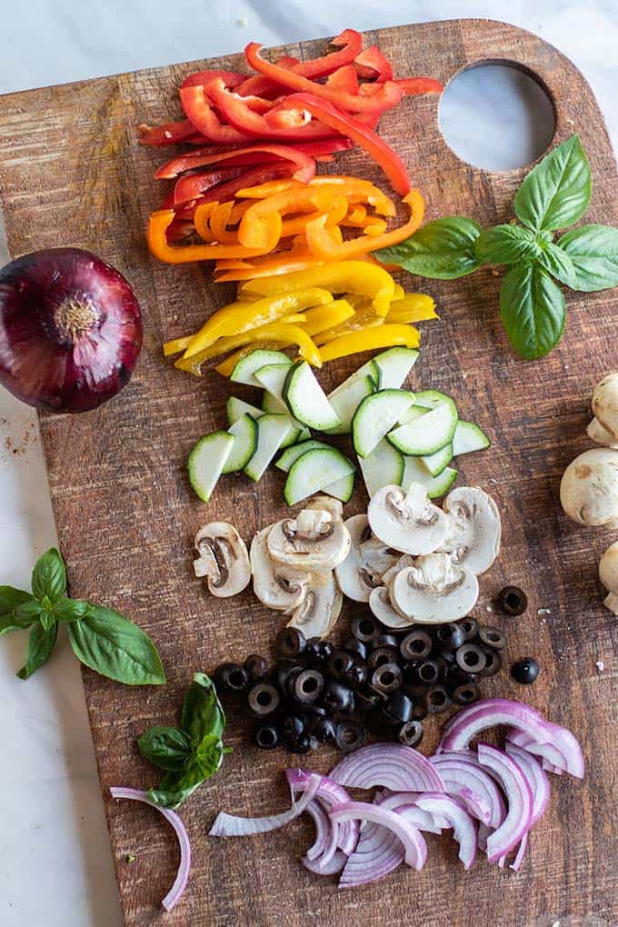A cutting board with a rainbow of veggies cut.