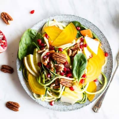 A whole30 zoodle salad topped with pears, pomegranate, beets and pecans.