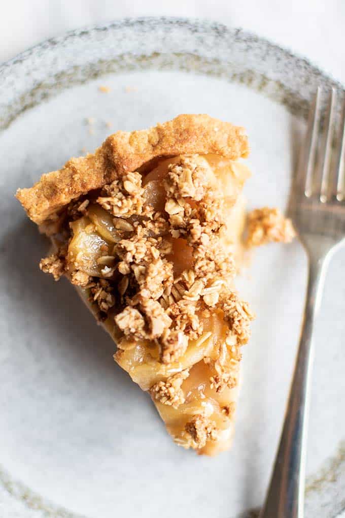 A piece of gluten free apple pie with a crumble topping on a plate with a fork.