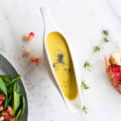 Tahini honey mustard salad dressing in a container next to a spinach salad.