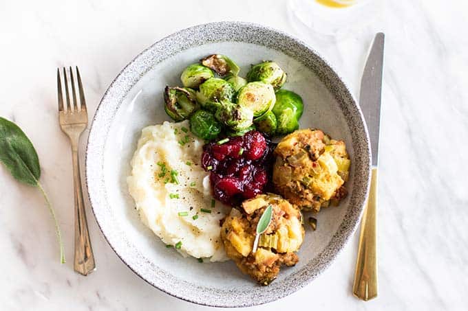 A plate with two sausage stuffing balls, with mashed cauliflower, cranberries and brussels sprouts.