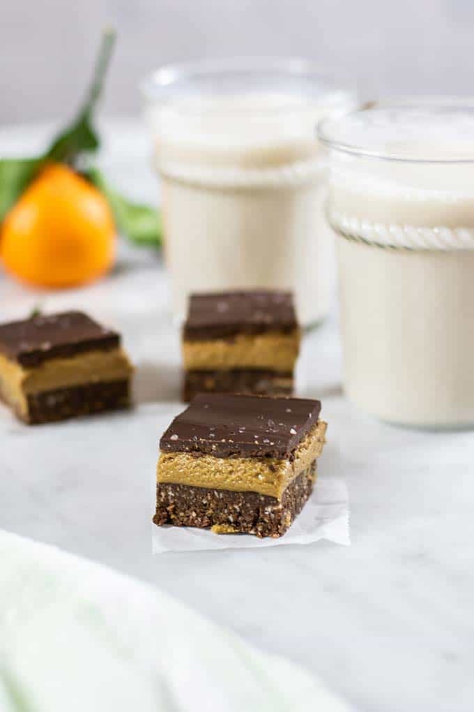 Nanaimo bars sitting on a counter with oranges and milk.