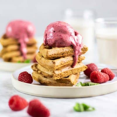 Stacks of gluten free waffles topped with beet and raspberry ice cream with glasses of almond milk.