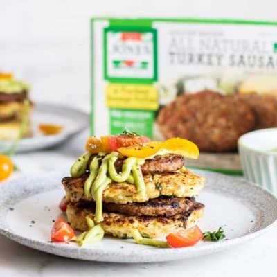 Cauliflower fritter and sausage stacks drizzled with avocado sauce and served with tomatoes.